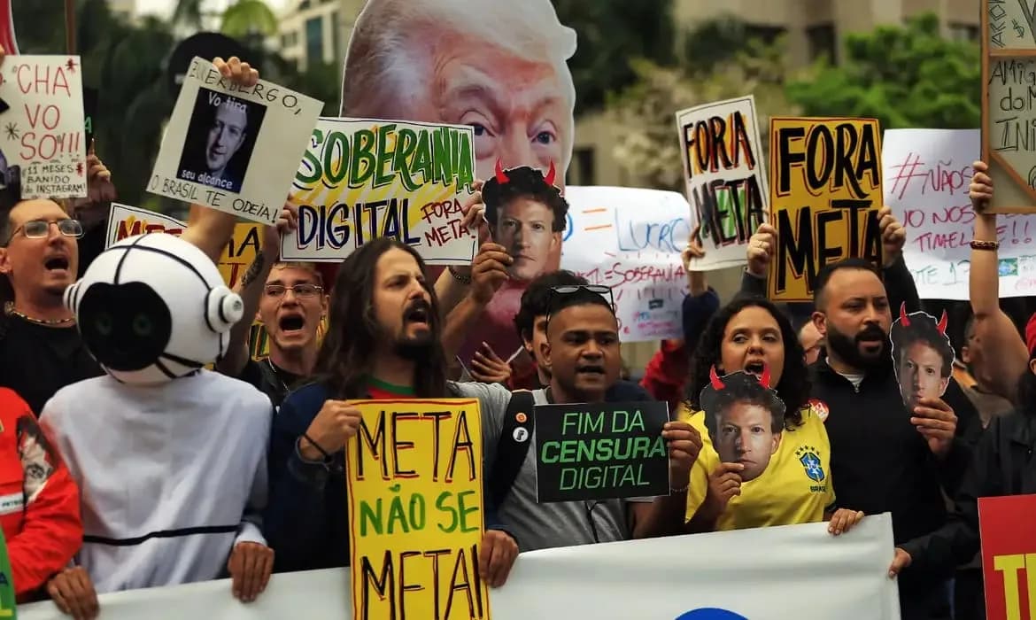 Manifestantes em protesto de rua seguram cartazes com os dizeres "Fora Meta", "Soberania digital", "Meta não se meta" e "Fim da censura digital", além de máscaras do rosto de Mark Zuckerberg com chifres e um grande recorte do rosto de Donald Trump